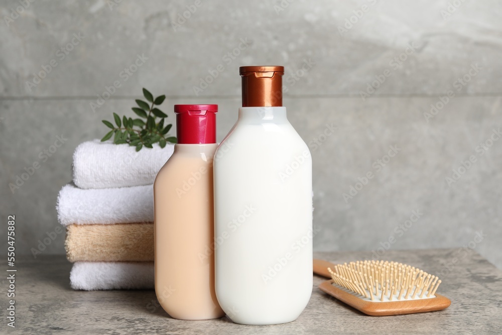 Bottles of shampoo, hairbrush and stacked towels on grey table Bottles of shampoo, hairbrush and stacked towels on grey table