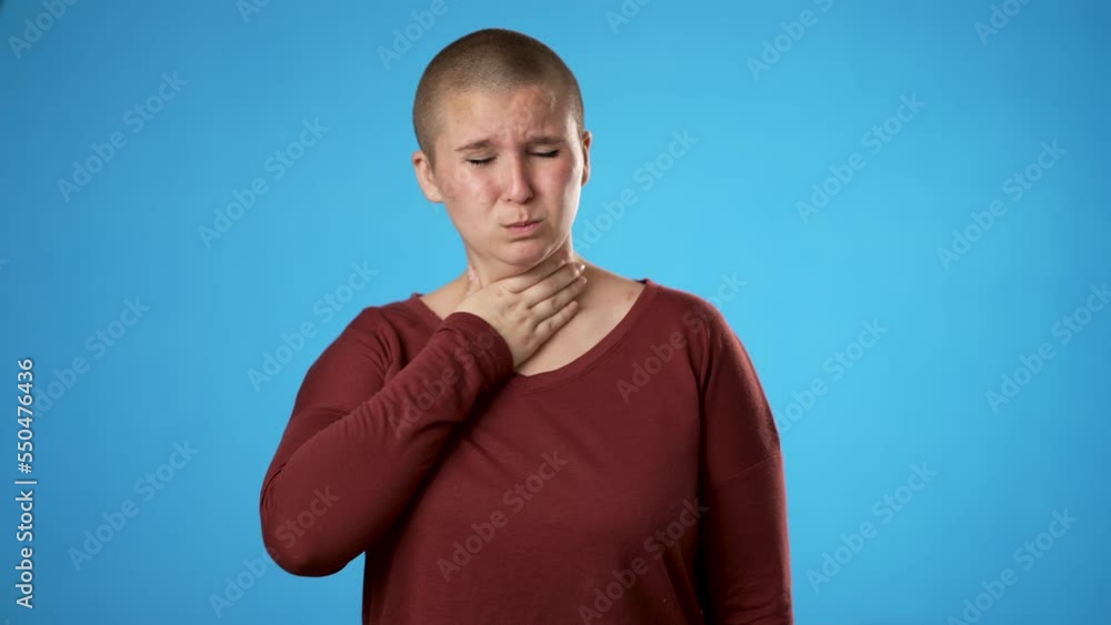 Portrait of gender fluid non binary young hipster woman 20s coughs into hand isolated on blue background studio. Healthy ill sick feel bad disease cold season Epidemic pandemic covid flu virus concept Portrait of gender fluid non binary young hipster woman 20s coughs into hand isolated on blue background studio. Healthy ill sick feel bad disease cold season Epidemic pandemic covid flu virus concept