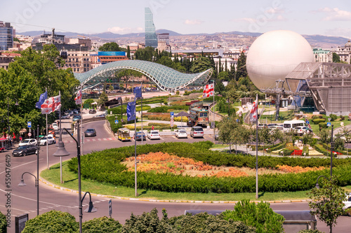 Summer day view along Noe Jordania Bank street in Avlabari neighborhood of Old Tbilisi with Bridge of Peace, huge baloon beside Aerial Tramway station in Rike park in foreground and two well-known photo