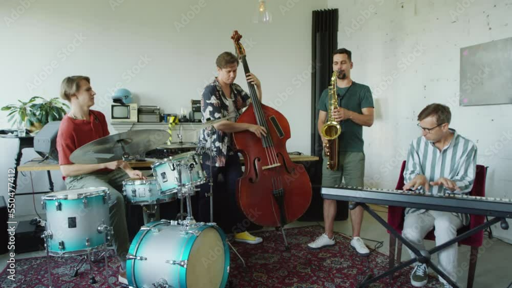 Wide shot of group of jazz musicians playing saxophone, synthesizer, double bass and drums together on rehearsal in studio Wide shot of group of jazz musicians playing saxophone, synthesizer, double bass and drums together on rehearsal in studio