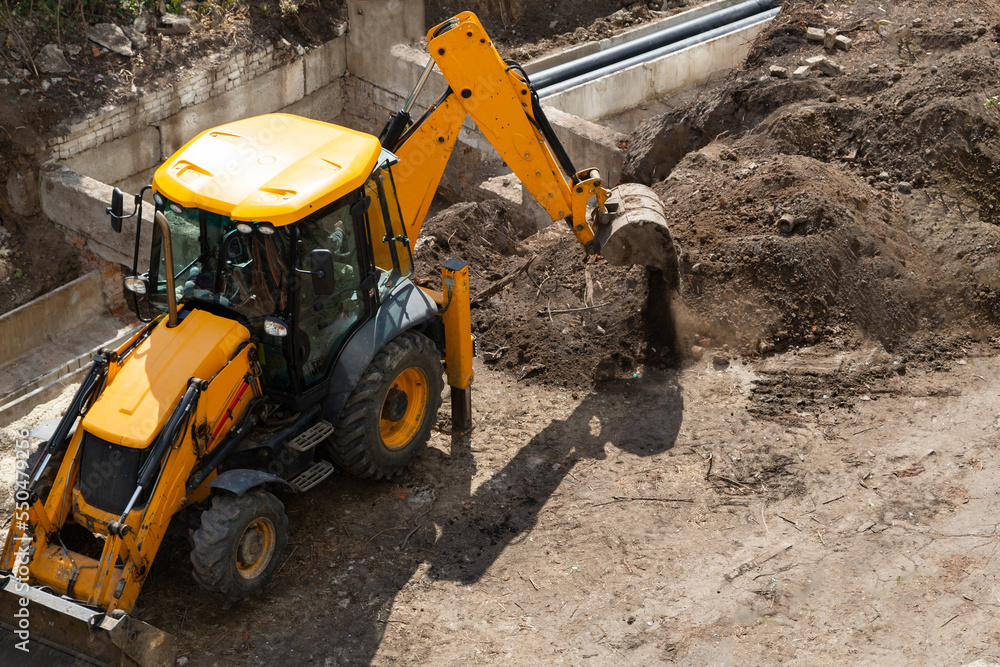An excavator digs the earth with a bucket at a construction site. An excavator digs the earth with a bucket at a construction site.