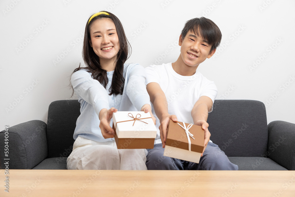 Happy attractive cheerful brother and sister or couple sitting on sofa holding a present box on birthday occasion or festival, teen care, love and relationship. Happy attractive cheerful brother and sister or couple sitting on sofa holding a present box on birthday occasion or festival, teen care, love and relationship.
