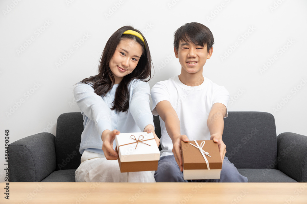 Happy attractive cheerful brother and sister or couple sitting on sofa holding a present box on birthday occasion or festival, teen care, love and relationship. Happy attractive cheerful brother and sister or couple sitting on sofa holding a present box on birthday occasion or festival, teen care, love and relationship.