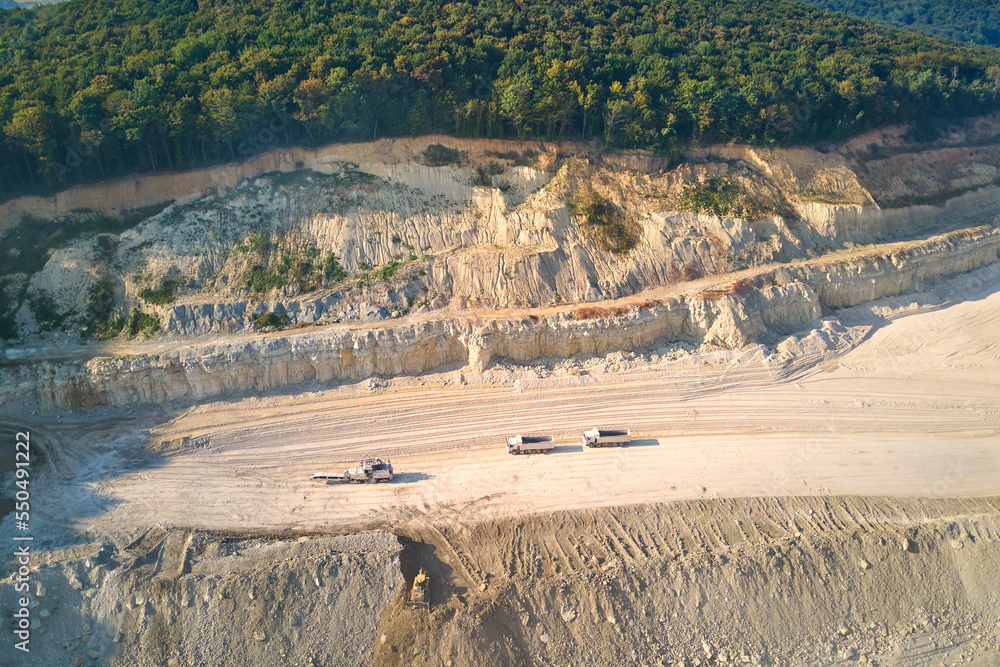 Aerial view of open pit mining of limestone materials for construction industry with excavators and dump trucks