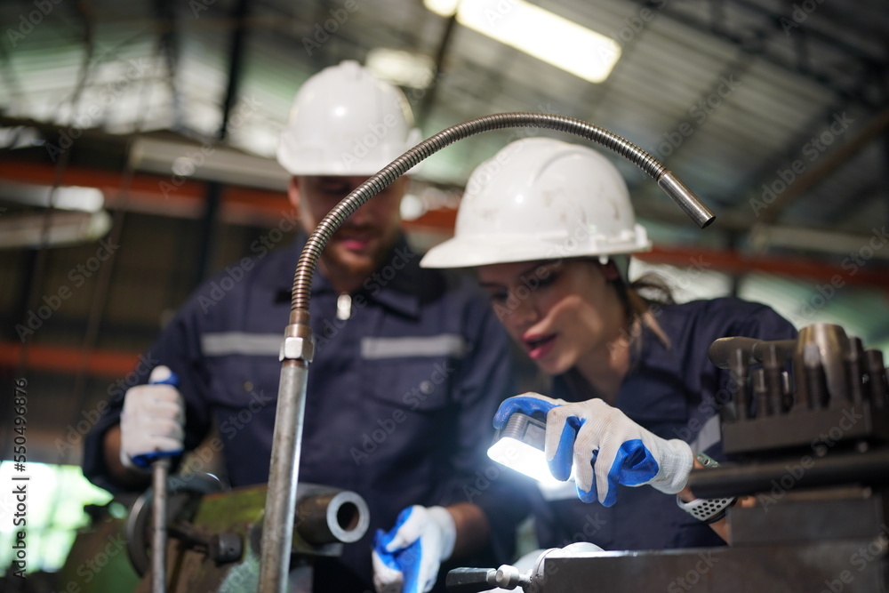 Young successful technician or repairman of industrial machines in safety helmet and workwear standing in large garage or workshop Young successful technician or repairman of industrial machines in safety helmet and workwear standing in large garage or workshop