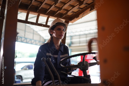 Young successful technician or repairman of industrial machines in safety helmet and workwear standing in large garage or workshop