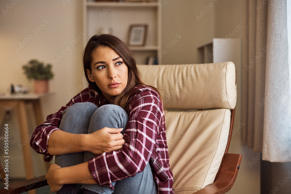 Young sad woman hugging her knees while sitting in armchair at home. Young sad woman hugging her knees while sitting in armchair at home.