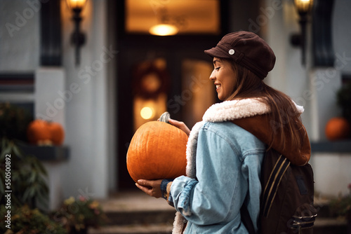 Young happy woman with pumpkin in front of her house.