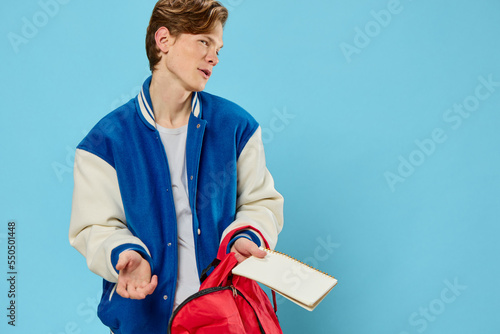 Tela a pensive student in a blue stylish bomber jacket stands with a notebook in his hands and looks away