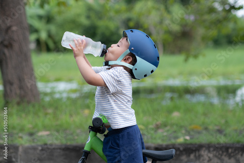 Cute Baby boy on a bike wearing helmet drinks water from water bottle