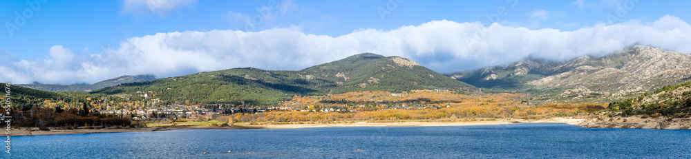 Navacerrada reservoir in autumn with the town in the background and the mountains of the Sierra de Guadarrama in Madrid