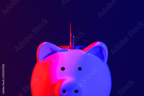Piggy bank with coin on a dark background red-blue backlight. Banking concept. Bright neon lights