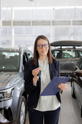woman sells a car at a car dealership and hands over the keys to the buyer. nice woman car sales manager. a successful and happy woman with a tablet in her hands is the head of a car dealership