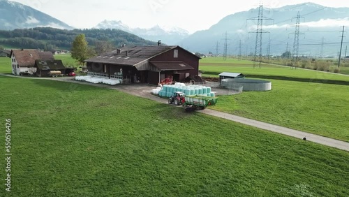 Tractor trolley filled with grains, reaching farmhouse amidst beautiful valley in Switzerland. photo