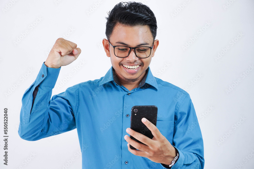 excited young asian employee man with glasses holding phone with clenched fists wearing blue shirt isolated on white background excited young asian employee man with glasses holding phone with clenched fists wearing blue shirt isolated on white background