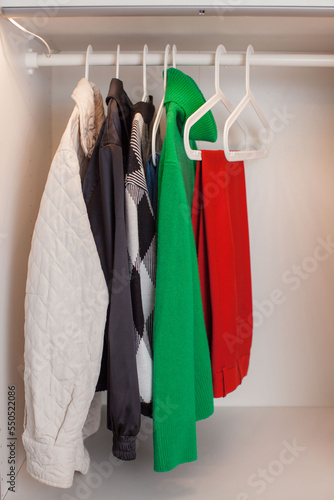 Trendy women's clothing hangs on white hangers in the wardrobe. Organized closet. Front view. 