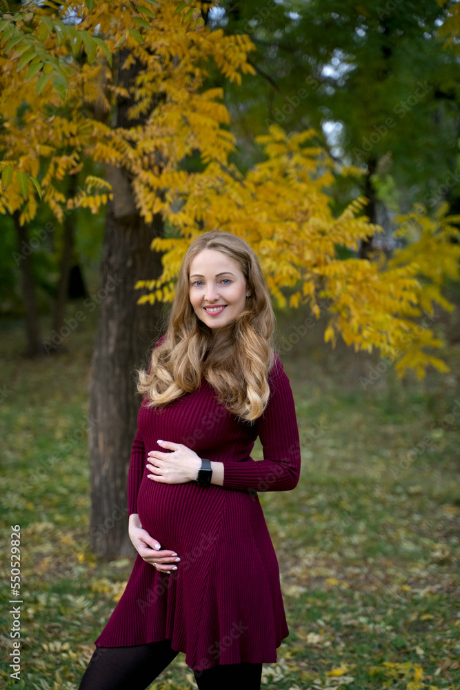 Pregnant girl in autumn forest smiling and holding her stomach