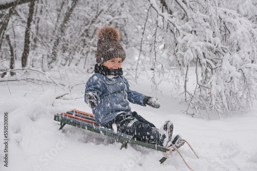 Little boy on a walk with a sled in a snowy winter.