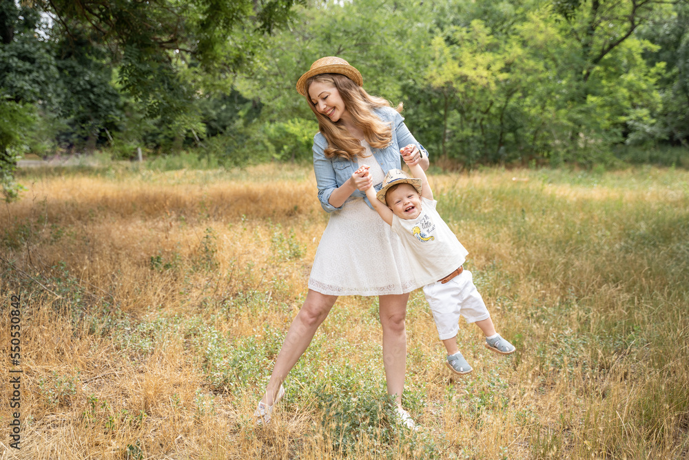 Fototapeta premium mother plays with her son in a meadow in the summer in straw hats