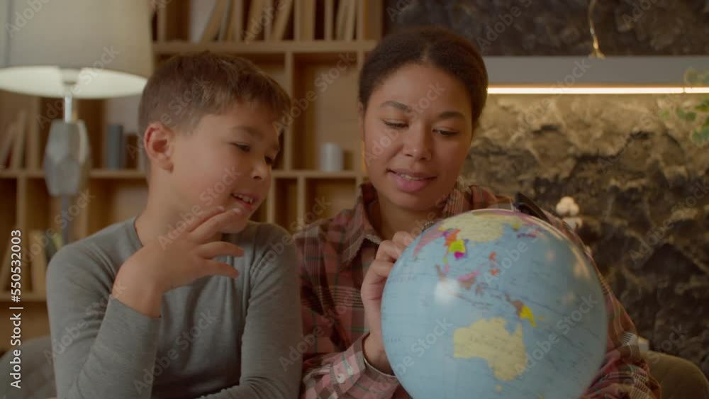 Portrait of adorable multiracial elementary age son and caring charming African American mother studying world with globe map, doing geography homework in domestic room. Portrait of adorable multiracial elementary age son and caring charming African American mother studying world with globe map, doing geography homework in domestic room.