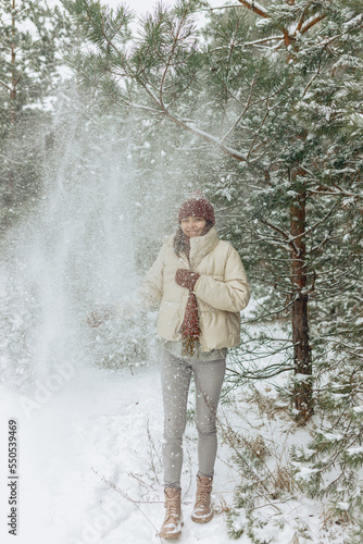 Happy woman having fun in winter forest while enjoying snow falling from tree 