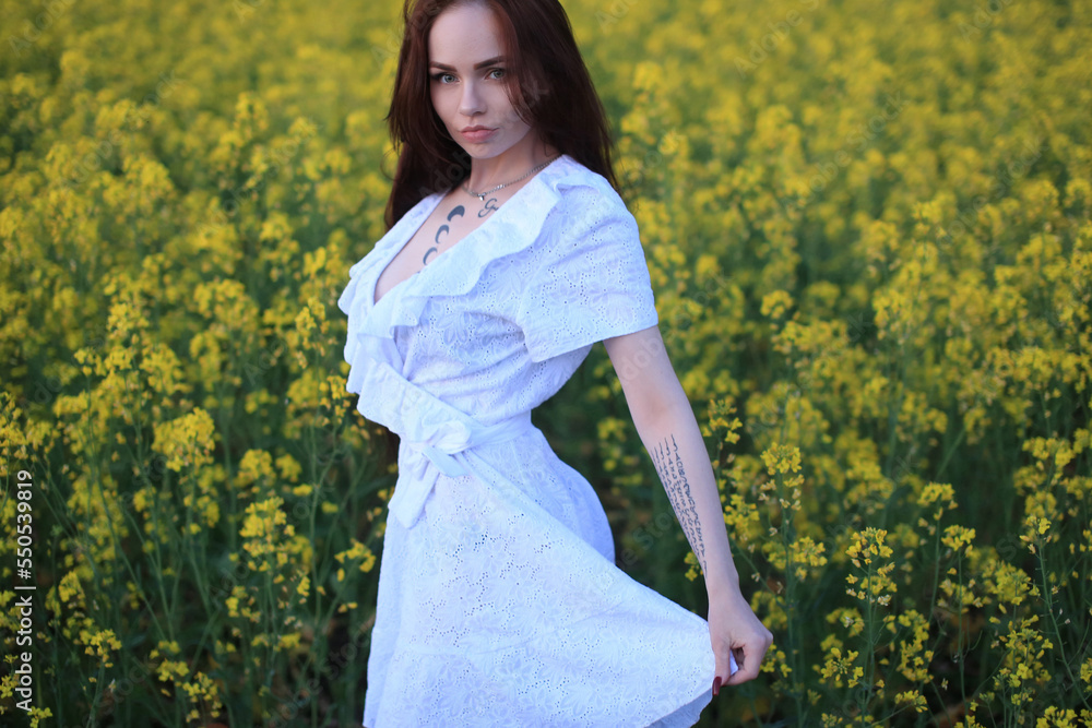 a beautiful fashionable girl with red hair stands in a rapeseed field in a white dress, with tattoos on her body against a background of yellow flowers a beautiful fashionable girl with red hair stands in a rapeseed field in a white dress, with tattoos on her body against a background of yellow flowers