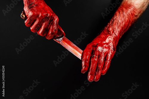A man wipes a bloody knife with his hand on a black background. 