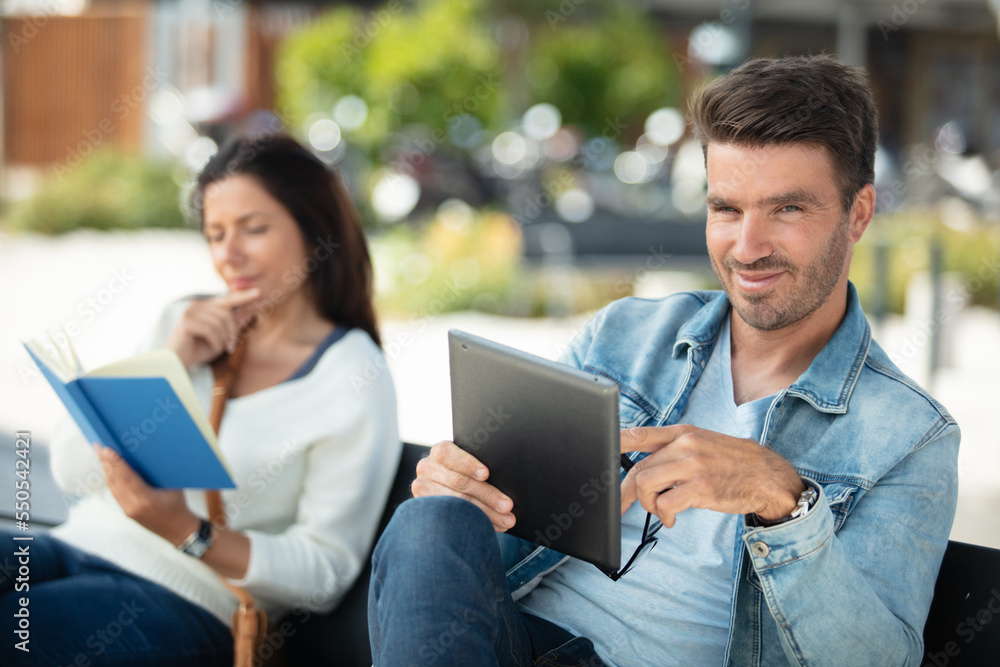 man using a tablet and woman with a book outdoors man using a tablet and woman with a book outdoors