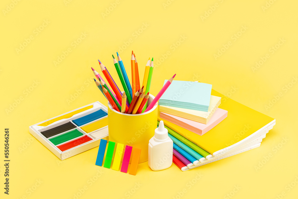 A set of stationery for school and office in the assortment. Notebooks, plasticine, pencils, scissors, eraser and glue on a bright yellow background. Side view.