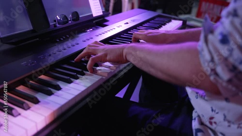 Close-up shot over the hands of a male musician playing peppy music in a synthesizer in a function in slow motion