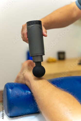 Physiotherapist doing a physiotherapeutic massage to the client on the leg with a machine with a round gun photo