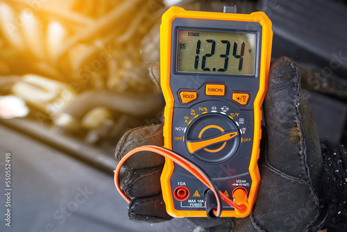 Checking car battery voltage. Mechanic check up car electric system with multimeter in cold winter conditions. Man with voltmeter measuring voltage level in car battery. Testing battery health photo