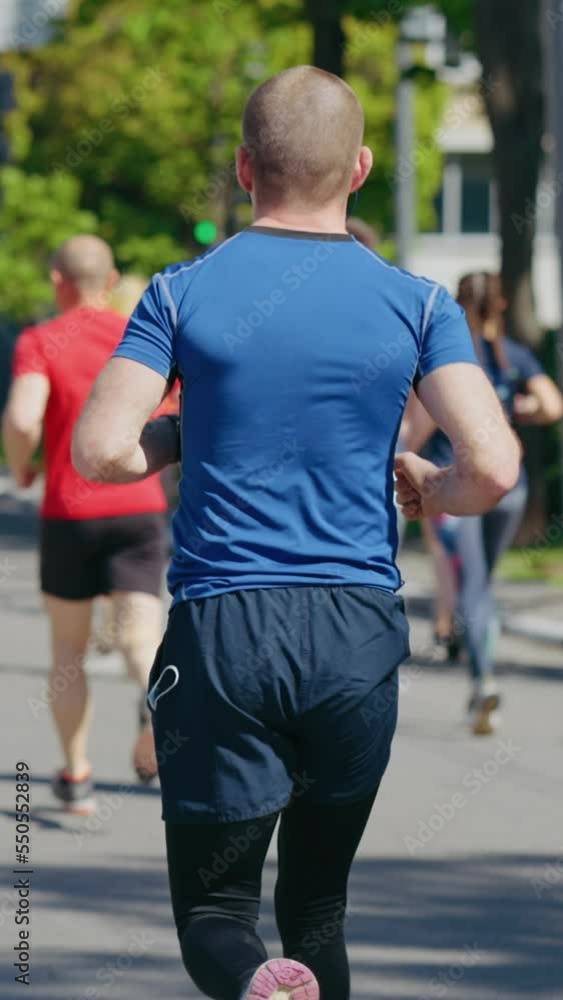 Vertical Screen: People running marathon in slow motion, focus on man with medical mask peeking out of his pocket. Back view crowd of contestants competing in sports event during pandemic Vertical Screen: People running marathon in slow motion, focus on man with medical mask peeking out of his pocket. Back view crowd of contestants competing in sports event during pandemic