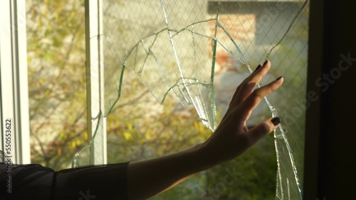 Hand moves across broken glass window photo