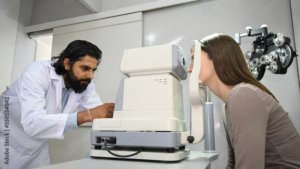 Image of caucasian woman checking eyesight on auto refractor in ophthalmologist clinic. Eye health check and ophthalmology concept