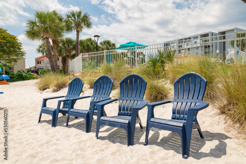 Destin, Florida- Four lounge arm chairs on a white sand near the beachgrass and fence