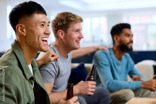 Group Of Excited Male Friends Watching Sports On TV At Home In Lounge Together