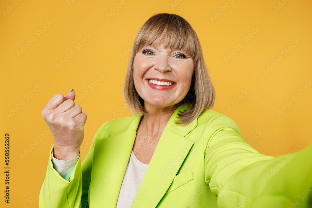 Close up elderly overjoyed happy woman 50s years old wear green jacket white t-shirt doing selfie shot pov on mobile cell phone do winner gesture isolated on plain yellow background studio portrait Close up elderly overjoyed happy woman 50s years old wear green jacket white t-shirt doing selfie shot pov on mobile cell phone do winner gesture isolated on plain yellow background studio portrait