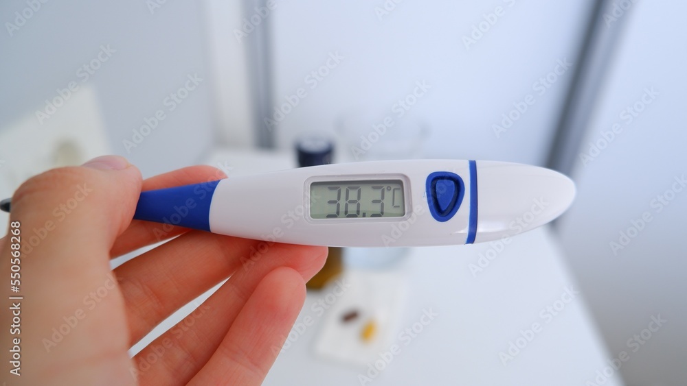 Checking temperature at home with digital thermometer, high body temperature, some medication on table to decrease fever, self monitoring, Health and Medical concept Checking temperature at home with digital thermometer, high body temperature, some medication on table to decrease fever, self monitoring, Health and Medical concept