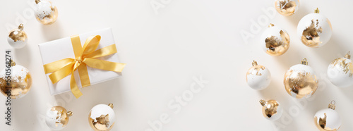 White Christmas banner with gift, gold plated balls on white background. Xmas greeting card with copy space. Modern luxury Christmas card. Happy New Year.