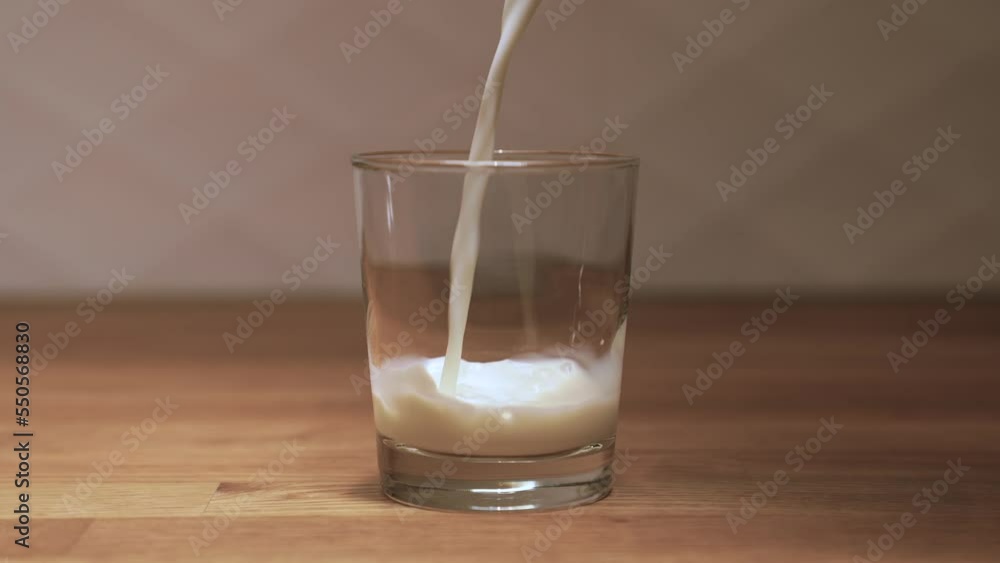 Slow motion shot of milk being poured into a glass on a wood table. SLO MO Pouring milk into a glass. Home kitchen. Slow motion shot of milk being poured into a glass on a wood table. SLO MO Pouring milk into a glass. Home kitchen.