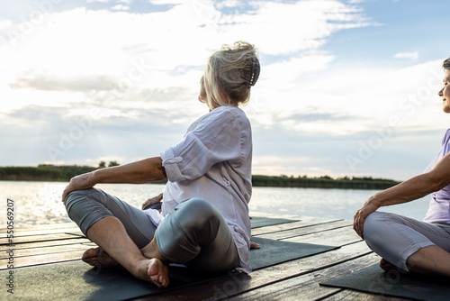 Group of senior woman doing yoga exercises by the lake.