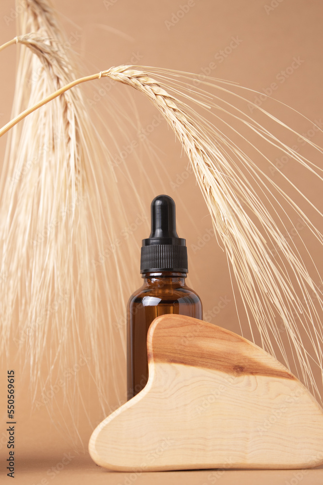 Fototapeta premium Bottle with lotion, serum, essential oil with wooden guasha on a beige background. Natural organic eco cosmetics. Natural cosmetics made from wheat and barley.