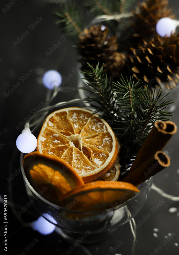 on a dark background, two transparent glasses with a New Year's decoration from oranges, cinnamon cones, a garland and a Christmas tree. for cards invitations labels calendars on a dark background, two transparent glasses with a New Year's decoration from oranges, cinnamon cones, a garland and a Christmas tree. for cards invitations labels calendars