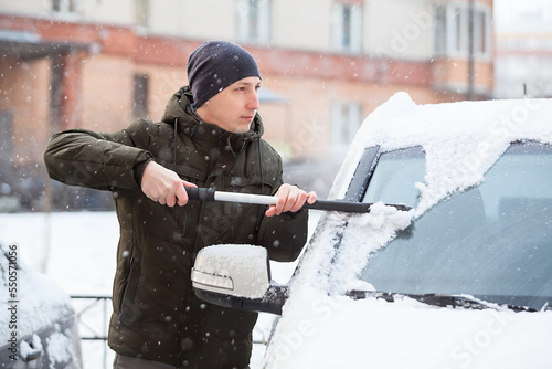 Man remove snow from the front of his car, sweeping from the glass of windshield