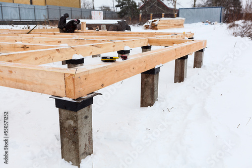 Corner of concrete pile foundation with floor board from square-sawn timber, several carpenters working photo