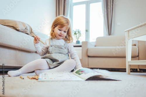 Little kid girl drawing at home creativity development. Talented artist. Inspired attentive little child girl sitting on warm floor in cozy apartment painting funny pictures with fiber-tip pens