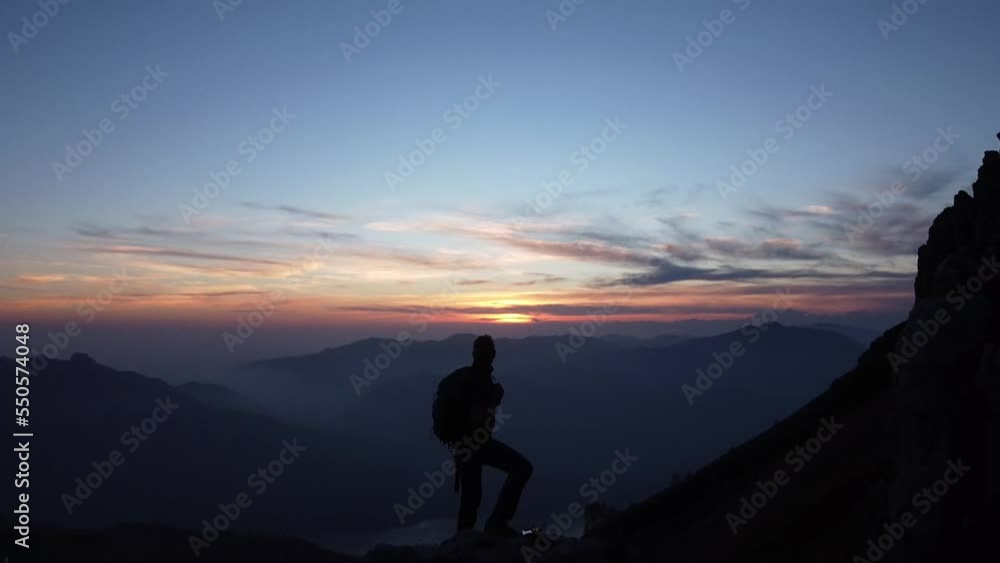 Hiker with backpack standing on top of mountain ridge at sunset Hiker with backpack standing on top of mountain ridge at sunset