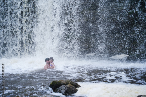 A little girl bathes with her dad under a waterfall in summer. day