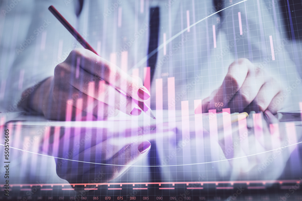 A woman hands writing information about stock market in notepad. Forex chart holograms in front. Concept of research. A woman hands writing information about stock market in notepad. Forex chart holograms in front. Concept of research.